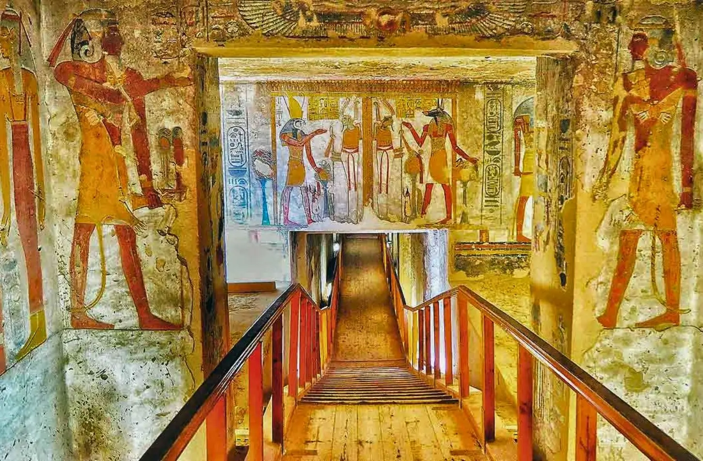Interior view of an ancient Egyptian tomb in the Valley of the Kings with colorful hieroglyphics and wall murals lining the entrance corridor.