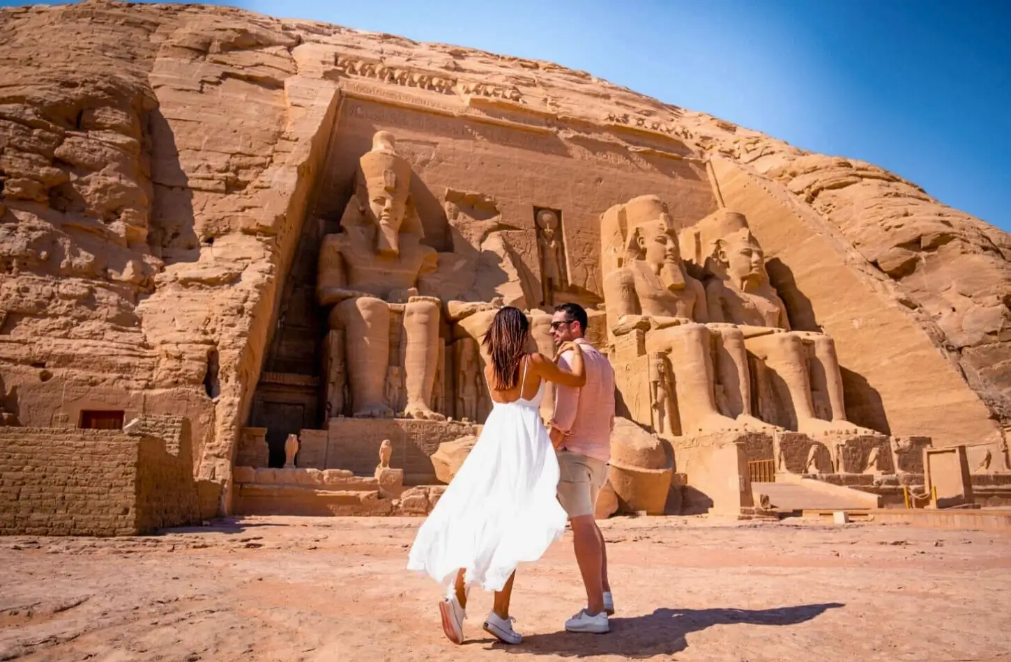 Muž a žena v bílém letním oblečení se dívají na masivní kamenné sochy faraonů v Abu Simbel, což je vrchol na jakémkoli seznamu Top 10 Must-See Temples in Egypt.