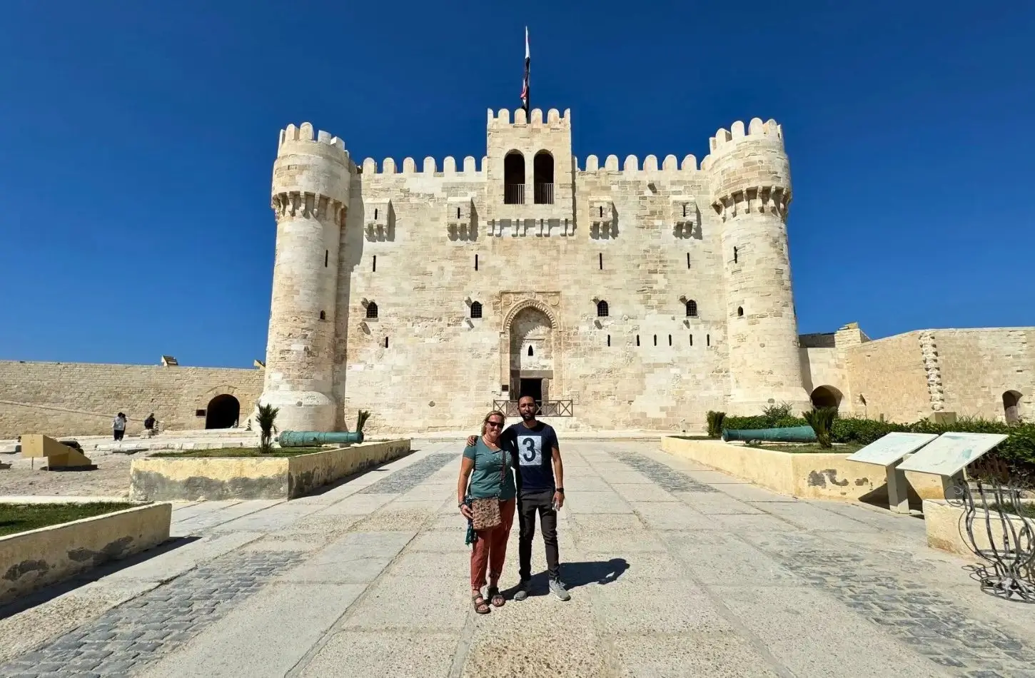 A couple posing in front of the historic Citadel of Qaitbay, a top destination featured in an Alexandria Travel Guide, under a bright blue sky.