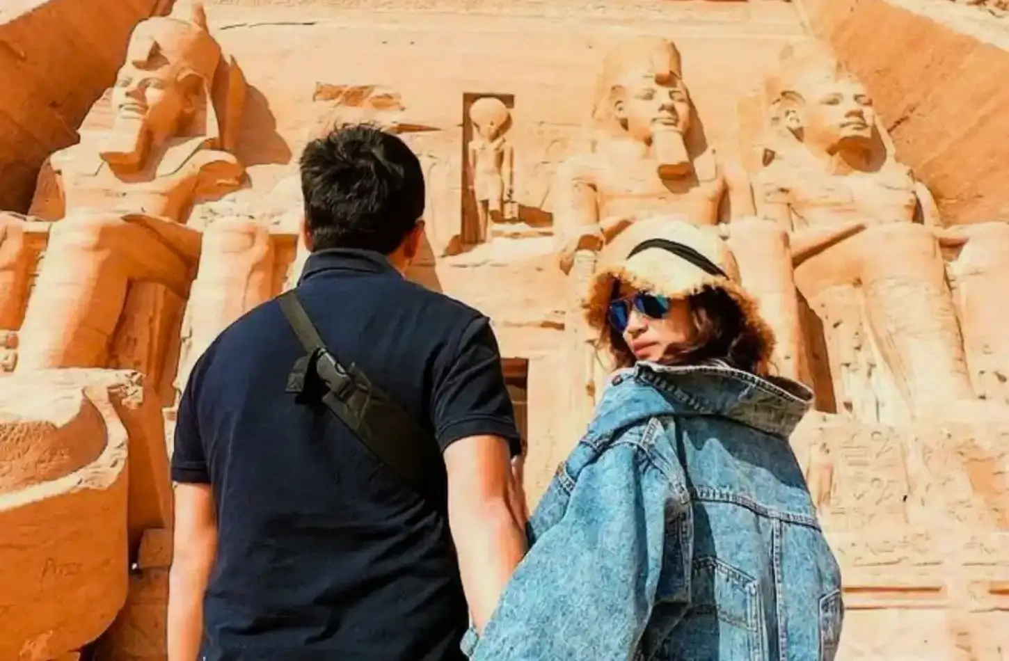 Pár, který se drží za ruce a dívá se na obrovské starověké sochy vytesané do fasády chrámů v Abu Simbel v Egyptě.