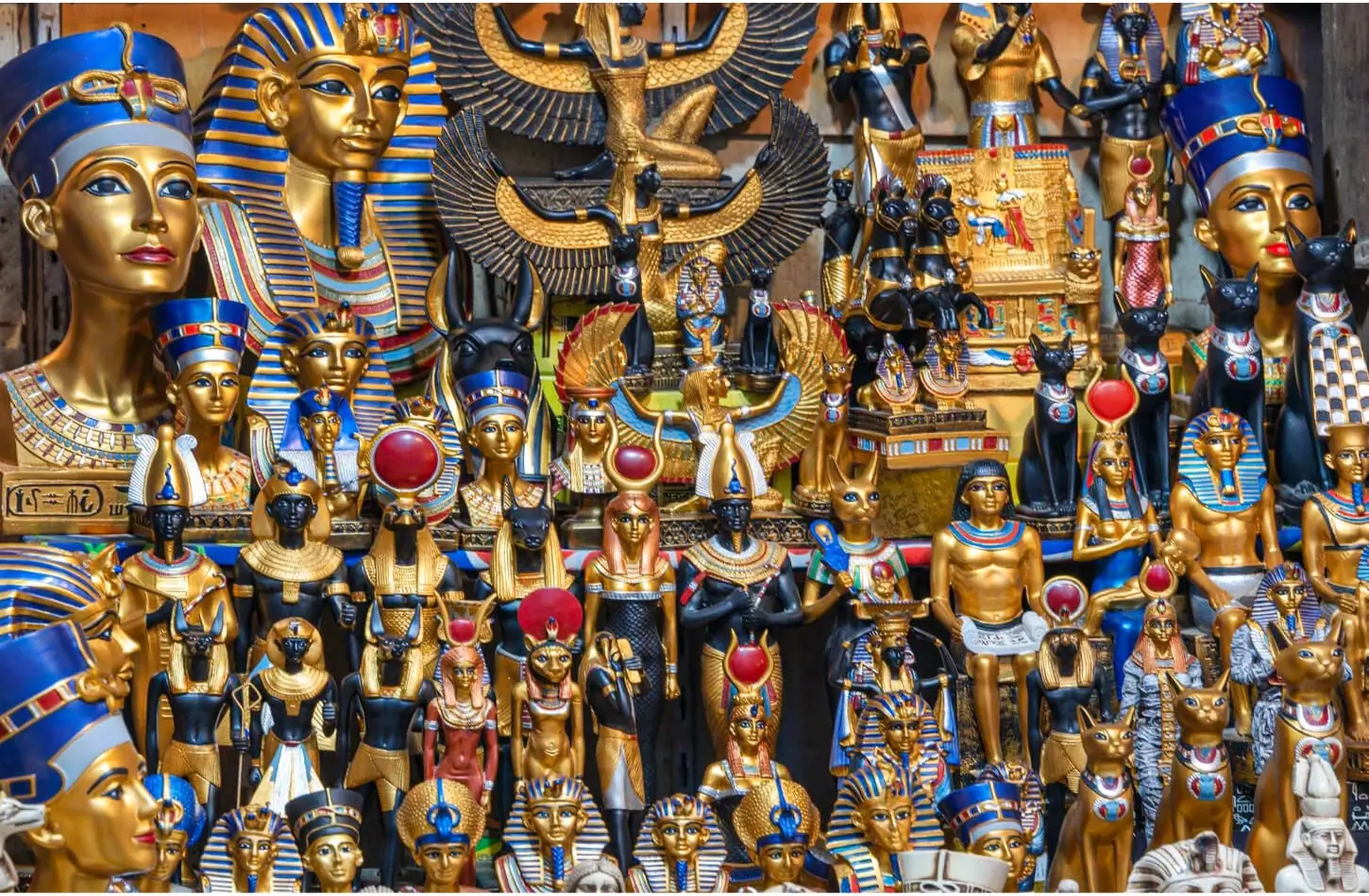 A vibrant display of golden and black Ancient Egyptian souvenir statues at a local bazaar, featuring replicas of King Tutankhamun’s mask, Queen Nefertiti busts, Anubis, and Bastet cats.
