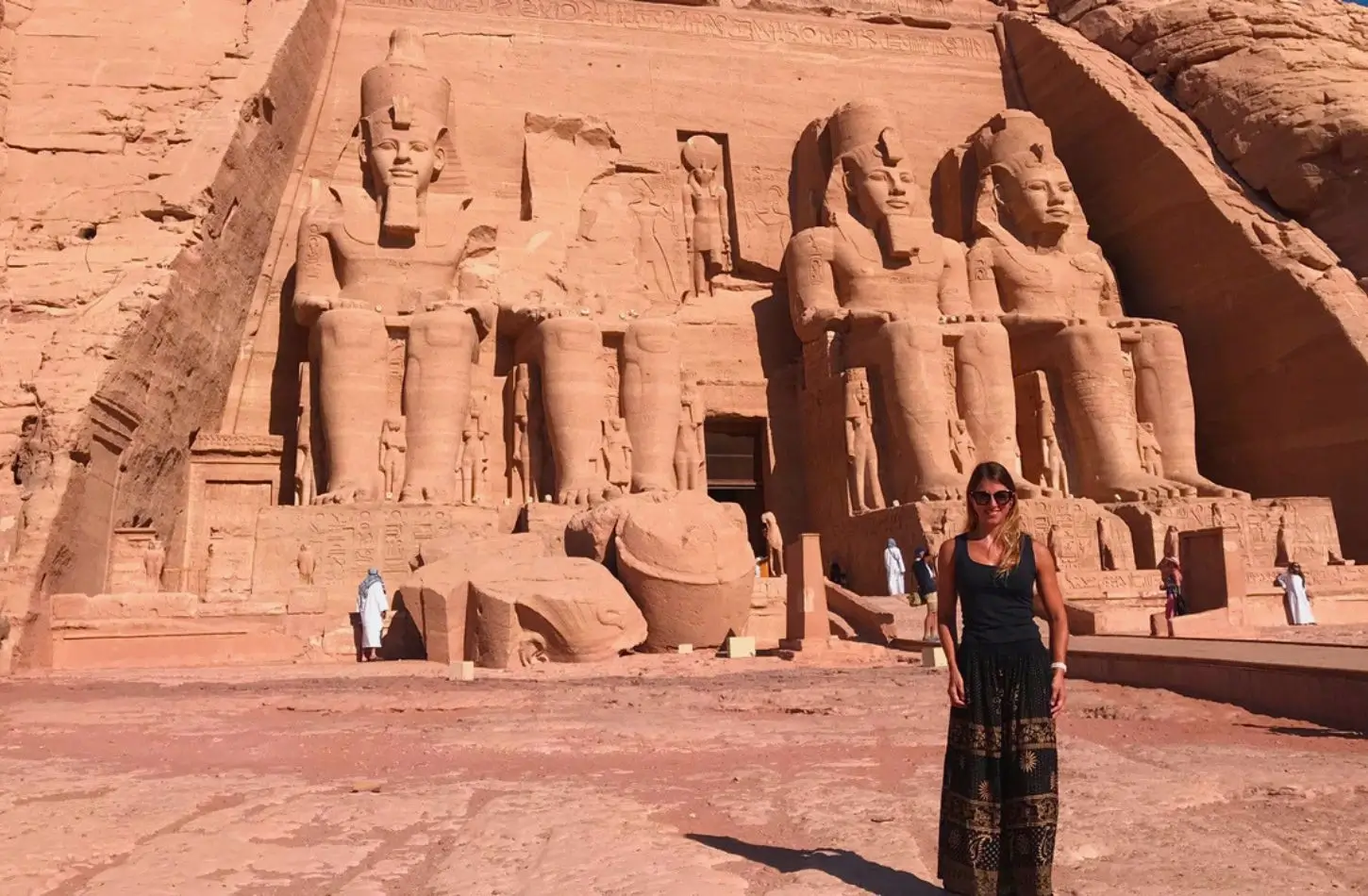 Žena se usmívá před obrovskými skalními sochami Ramese II. v chrámech Abu Simbel, oblíbená destinace při zkoumání, jak naplánovat cestu do Egypta.