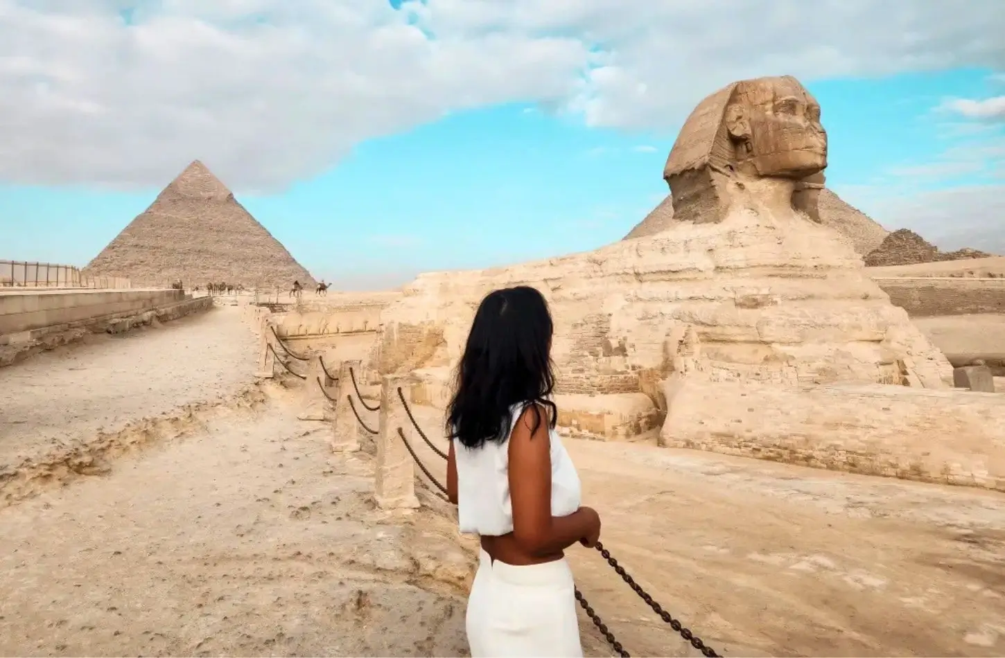 Cestovatel v bílém oblečení se dívá na Velkou sfingu a pyramidu v Gíze, což je nezbytná zastávka v každém průvodci po Káhiře.