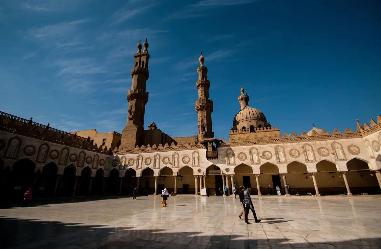 The sunny open marble courtyard of Al-Azhar Mosque in Islamic Cairo, featuring its historic stone minarets, central dome, and arched porticos under a deep blue sky, perfect for a Marsa Alam excursion