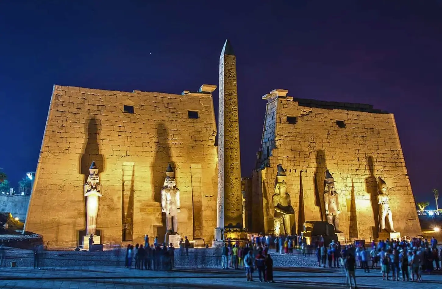 Velkolepý vchod do chrámu Luxor v noci, krásně osvětlený velkými staroegyptskými sochami a obeliskem.