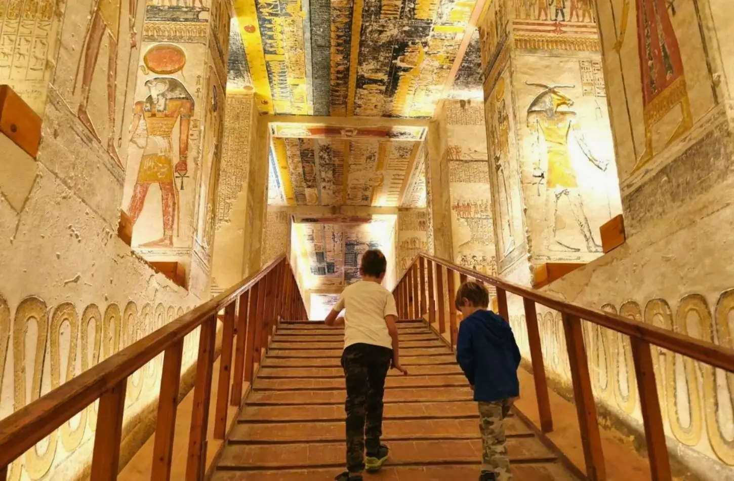 Valley of the Kings tomb interior with colorful ancient Egyptian wall paintings and visitors exploring the decorated burial chambers.