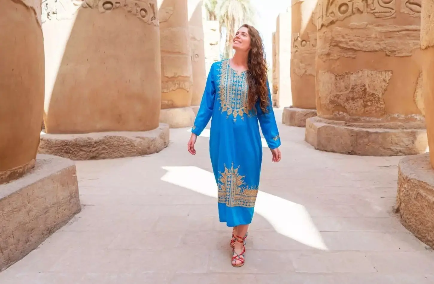 Woman in a traditional blue dress walking through the historic stone columns of Karnak Temple in Egypt.
